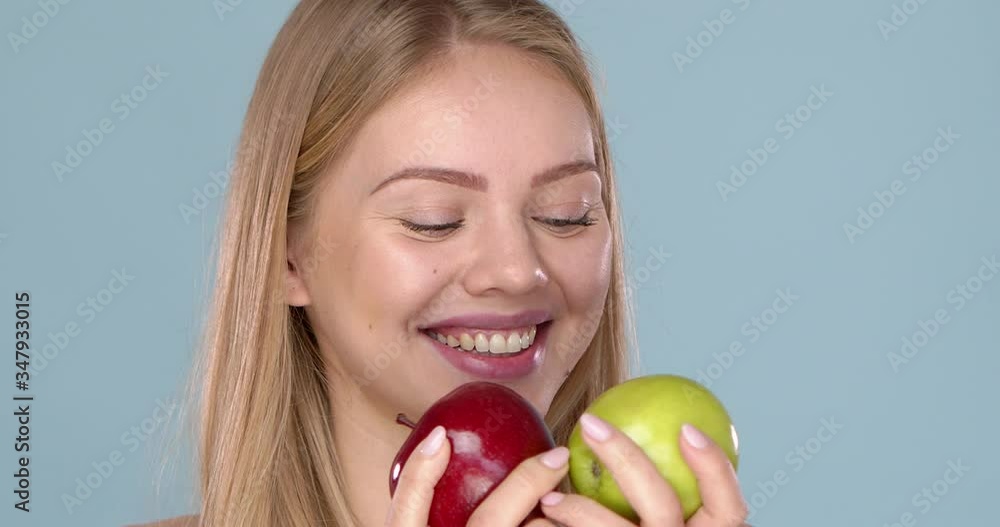 Close up studio shot of smiling young woman holding two apples, red and green Close up studio shot of smiling young woman holding two apples, red and green