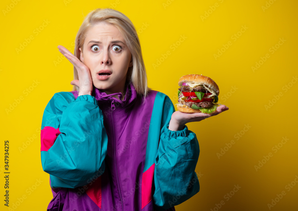 surprsied girl in 80s clothes style with burger on yellow background surprsied girl in 80s clothes style with burger on yellow background