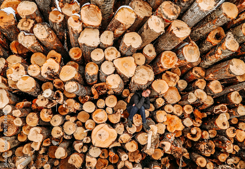 man sits alone on stack pile of cut logs with chin on hand man sits alone on stack pile of cut logs with chin on hand