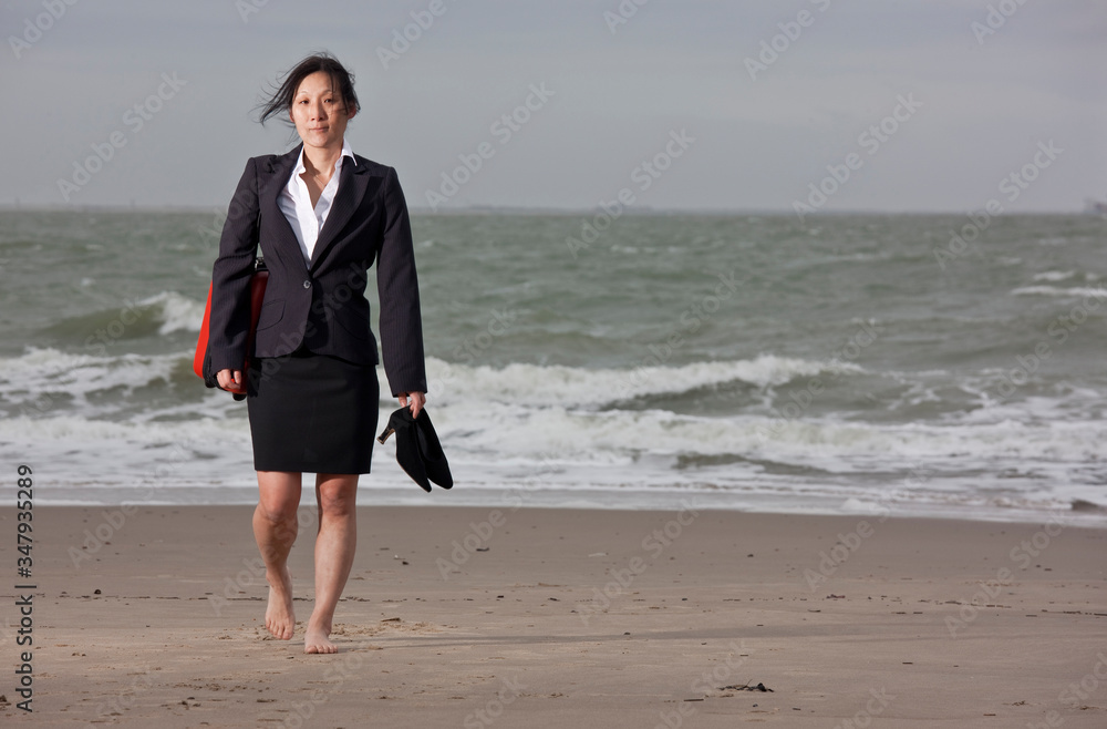 business woman walking on empty beach holding her shoes business woman walking on empty beach holding her shoes