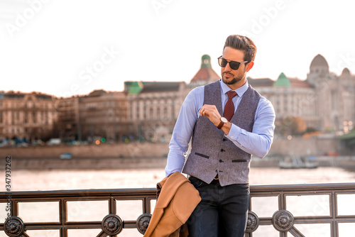 An elegant man standing next to a river and checking the time