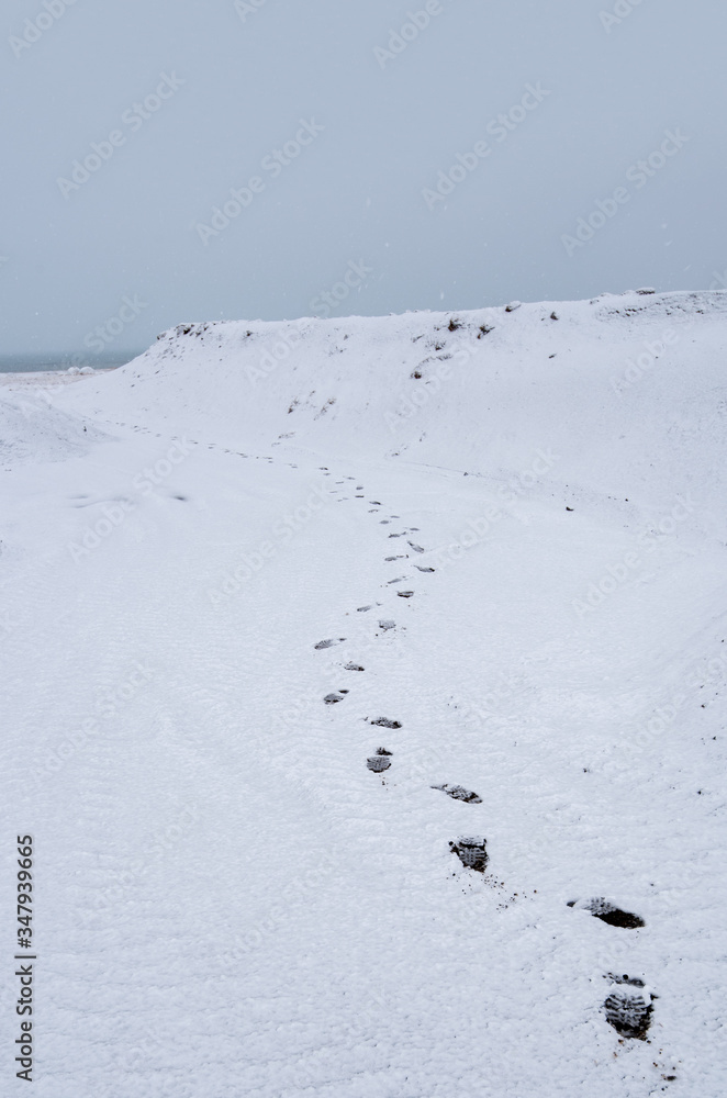 Human footprints on a snowy hill leading to the sea