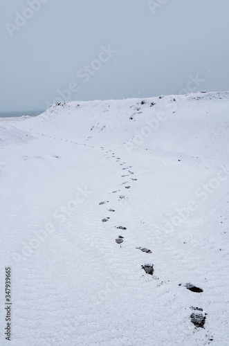 Human footprints on a snowy hill leading to the sea