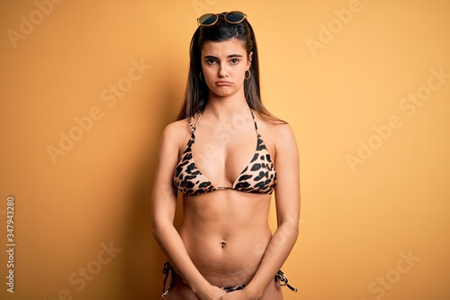 Young beautiful brunette woman on vacation wearing swimwear bikini over yellow background depressed and worry for distress, crying angry and afraid. Sad expression.