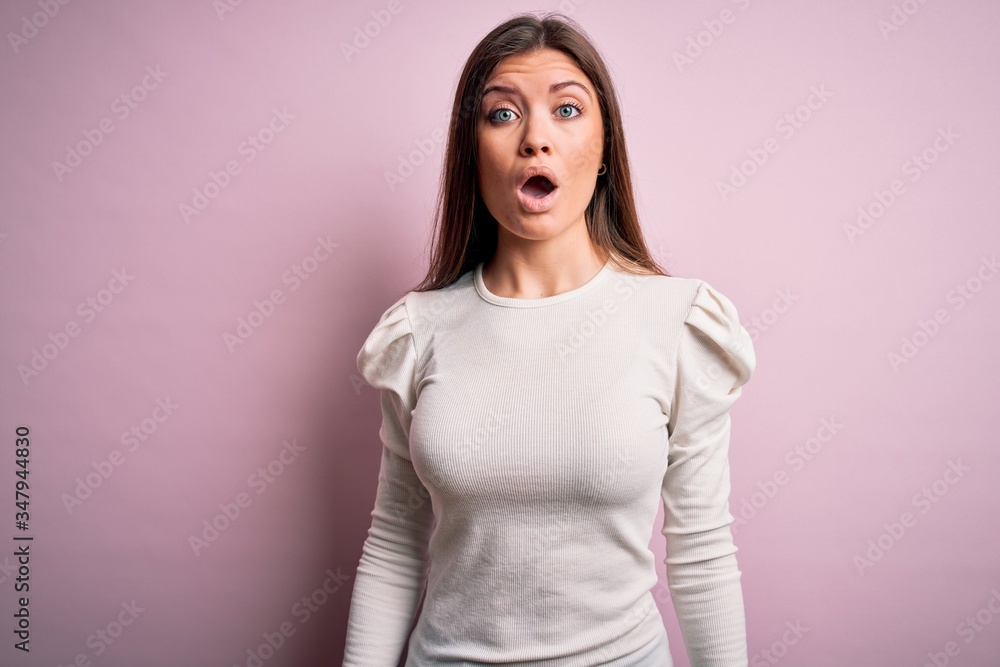 Obraz premium Young beautiful woman with blue eyes wearing casual white t-shirt over pink background afraid and shocked with surprise and amazed expression, fear and excited face.