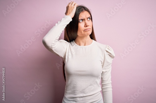 Young beautiful woman with blue eyes wearing casual white t-shirt over pink background confuse and wondering about question. Uncertain with doubt  thinking with hand on head. Pensive concept.