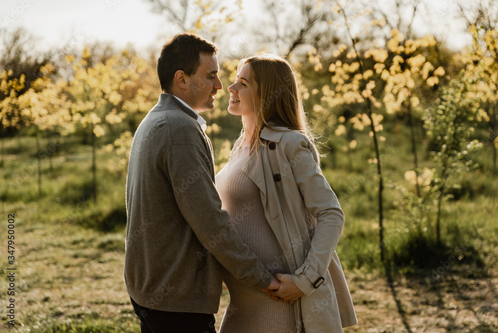 happy young pregnant couple walks in the park,husband holds the hand of his pregnant wife,future dad and mom,walks in the park after quarantine