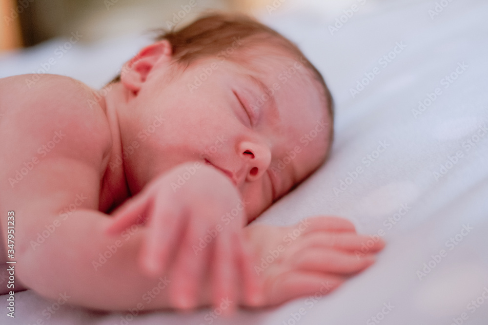 Calm cute infant with closed eyes covered with blanket resting in bed against blurred interior of light bedroom Calm cute infant with closed eyes covered with blanket resting in bed against blurred interior of light bedroom