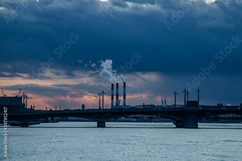 View of the smoking chimneys of a thermal power plant the Annunciation Bridge and the Neva River at beautiful sunset. Saint-Petersburg, Russia.