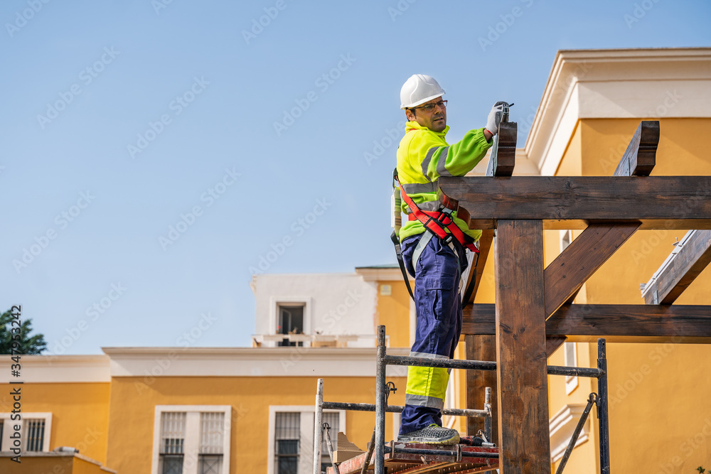 From below side view of male technician in work wear standing on scaffolding and preparing for installation of solar panel on wooden construction From below side view of male technician in work wear standing on scaffolding and preparing for installation of solar panel on wooden construction
