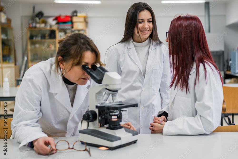 Woman using microscope near colleagues in laboratory