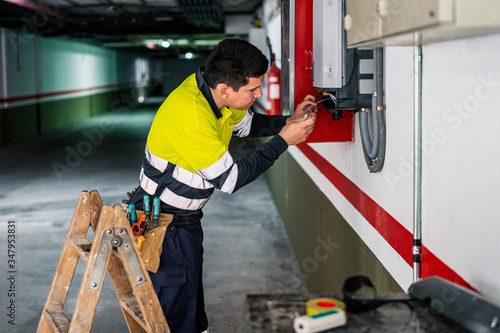 Side view of young professional male technician with electric tools repairing and checking equipment while working in building photo