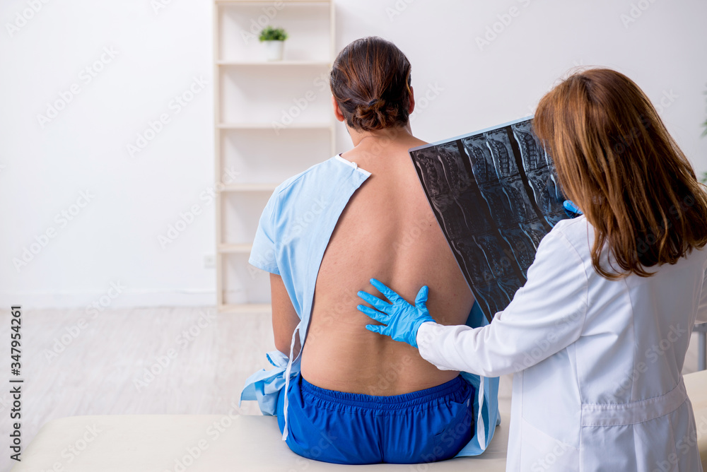 Obraz premium Young back injured man visiting female doctor chiropractor