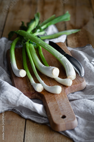 Bunch of ripe scallions placed on wooden cutting board and cloth napkin on rustic table in kitchen