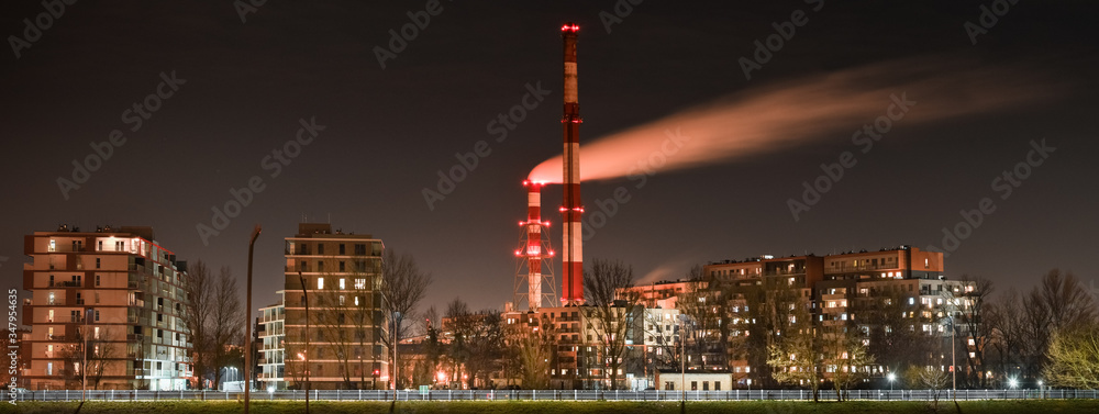 Fototapeta premium Night view of the smoke coming out of the chimney over apartment blocks in the city.