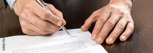 Canvas Print A businessman sits at an office Desk and signs a contract with a ballpoint pen