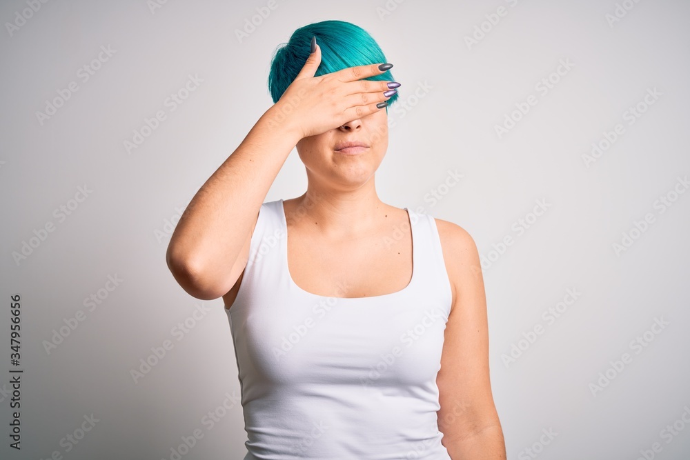 Young beautiful woman with blue fashion hair wearing casual t-shirt over white background covering eyes with hand, looking serious and sad. Sightless, hiding and rejection concept Young beautiful woman with blue fashion hair wearing casual t-shirt over white background covering eyes with hand, looking serious and sad. Sightless, hiding and rejection concept