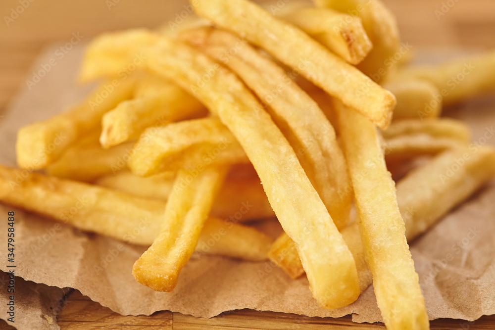 French fries in a paper on wooden table. Close up French fries in a paper on wooden table. Close up