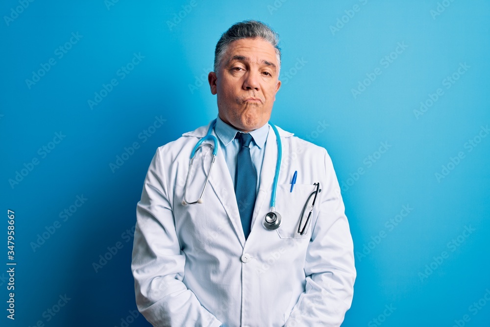 Middle age handsome grey-haired doctor man wearing coat and blue stethoscope looking sleepy and tired, exhausted for fatigue and hangover, lazy eyes in the morning. Middle age handsome grey-haired doctor man wearing coat and blue stethoscope looking sleepy and tired, exhausted for fatigue and hangover, lazy eyes in the morning.