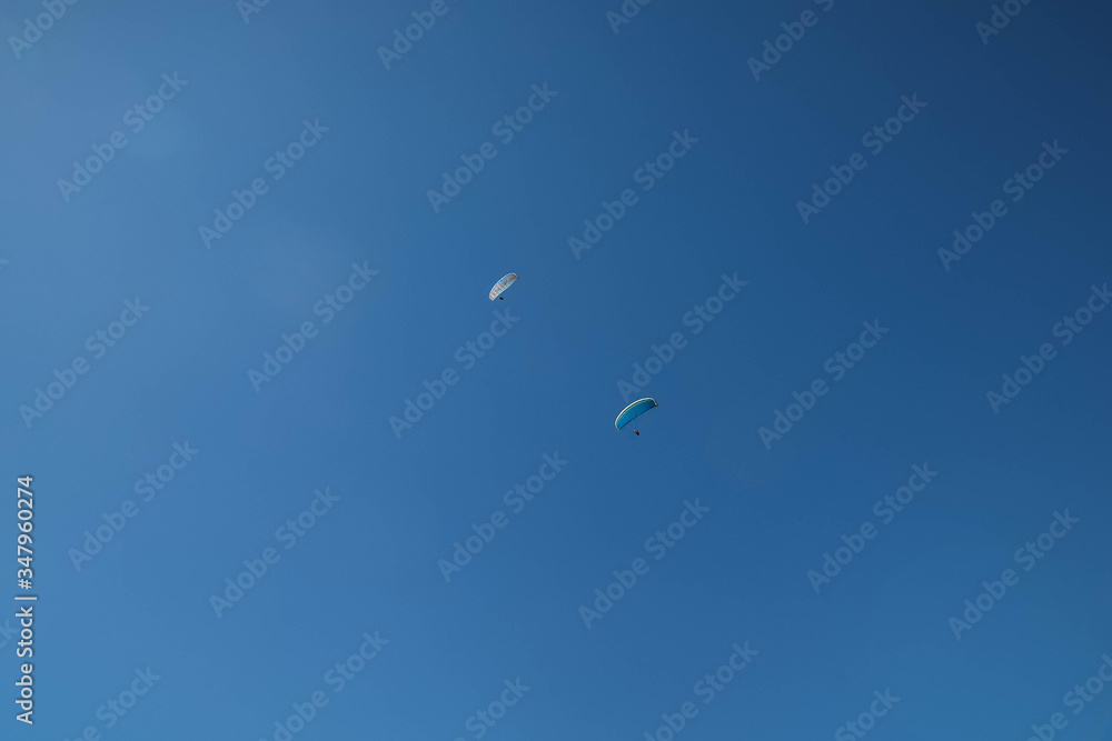 Two skydivers parachuting in the bright blue sky, looking up from below Two skydivers parachuting in the bright blue sky, looking up from below
