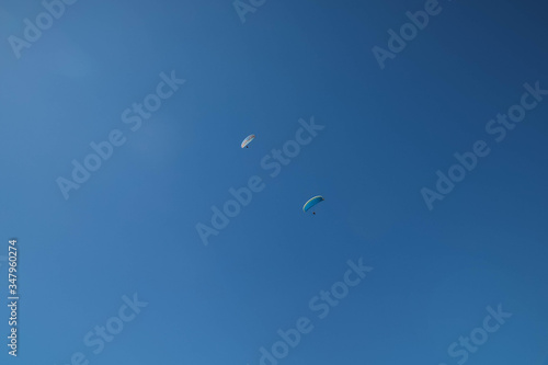 Two skydivers parachuting in the bright blue sky, looking up from below