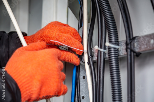 Hands with gloves fasten the cable ties on the cable, which are on the cable tray. Close-up. Horizontal orientation.