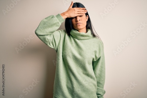 Young beautiful hispanic woman wearing green winter sweater over isolated background covering eyes with hand, looking serious and sad. Sightless, hiding and rejection concept © Krakenimages.com