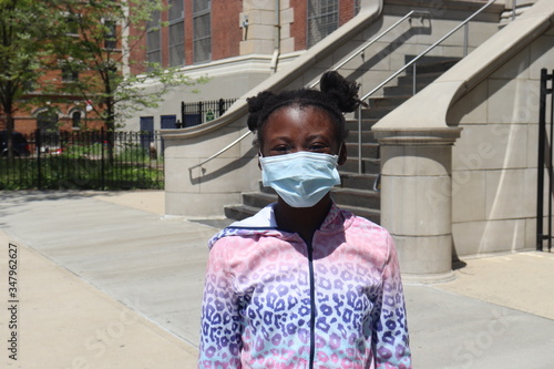 Preteen wearing mask covering outside standing on sidewalk with tall staircase background photo