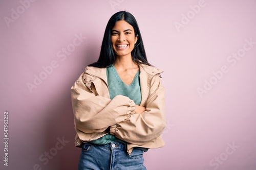Young beautiful hispanic fashion woman wearing winter jacket and sweater over pink background happy face smiling with crossed arms looking at the camera. Positive person. © Krakenimages.com