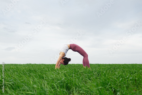 Young slim girl doing yoga outdoors in a green field