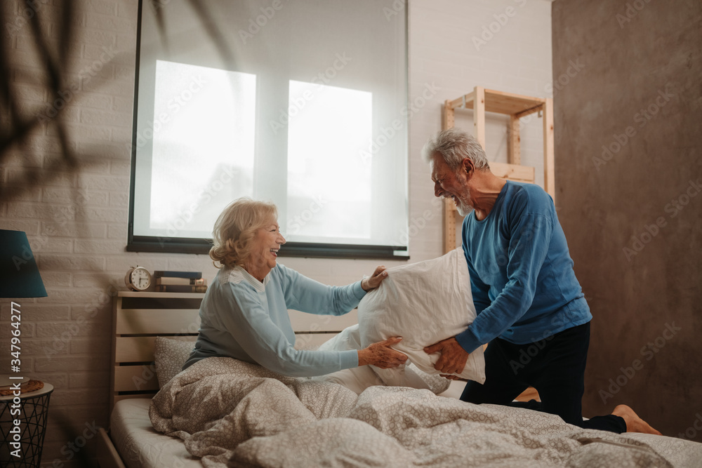 Happy elderly couple having a pillow fight on bed in their bedroom. Happy elderly couple having a pillow fight on bed in their bedroom.
