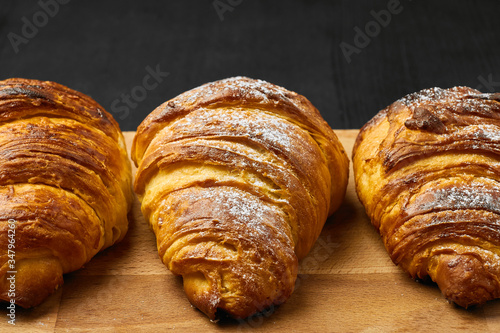 Three croissants with sugar powder on a wooden desk on a black background. Homemade baking concept.