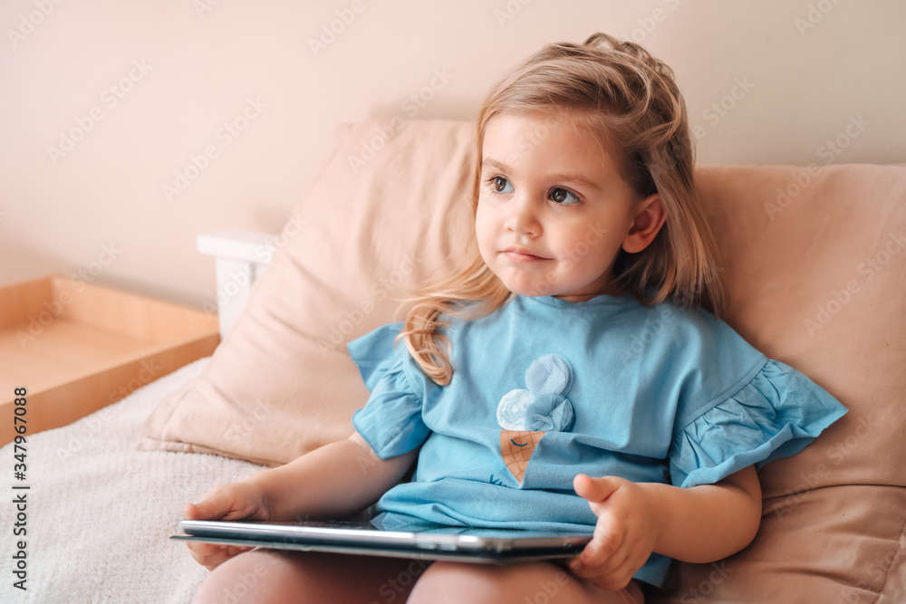 Beautiful child little girl playing with a tablet while lying on bed at home. Beautiful child little girl playing with a tablet while lying on bed at home.
