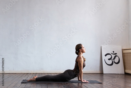 Young and fit woman practicing yoga indoor in the class. Stretching exercise in the day light. Sport, fitness, health care and lifestyle.
