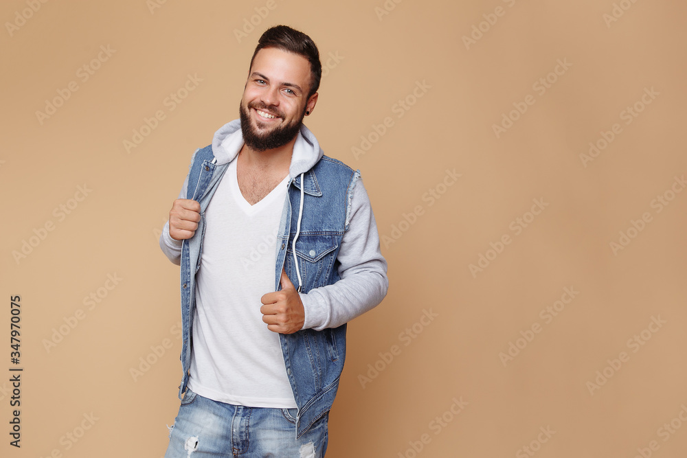 Stylish young cheerful guy with a beautiful beard in a denim jacket and white t-shirt on a plain cream background. Denim jacket advertising concept for billboard Stylish young cheerful guy with a beautiful beard in a denim jacket and white t-shirt on a plain cream background. Denim jacket advertising concept for billboard