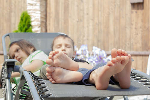 Upset children with children's bare feet on a chaise longue. a boy and a girl are resting in the sun. The concept of relaxation.
