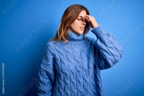 Young beautiful brunette woman wearing casual turtleneck sweater over blue background tired rubbing nose and eyes feeling fatigue and headache. Stress and frustration concept.