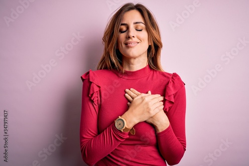 Young beautiful brunette woman wearing casual sweater stnding over pink background smiling with hands on chest with closed eyes and grateful gesture on face. Health concept. photo