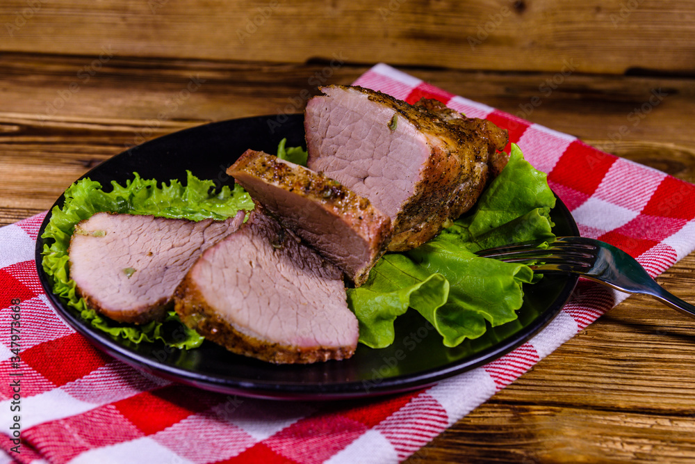 Slices of baked pork meat and lettuce leaves on a black plate Slices of baked pork meat and lettuce leaves on a black plate