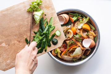 Vegetable peels are thrown from cutting board into an iron bowl with organic food waste. Food leftovers ready to compost. Environmentally responsible behavior, ecological, recycling waste concept.