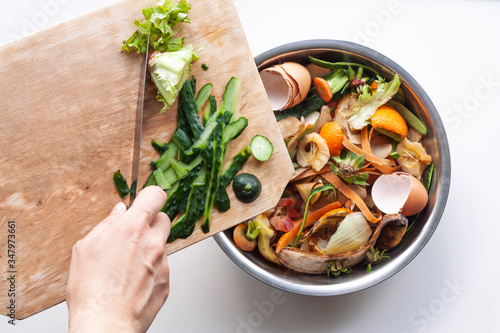 Vegetable peels are thrown from cutting board into an iron bowl with organic food waste. Food leftovers ready to compost. Environmentally responsible behavior, ecological, recycling waste concept.