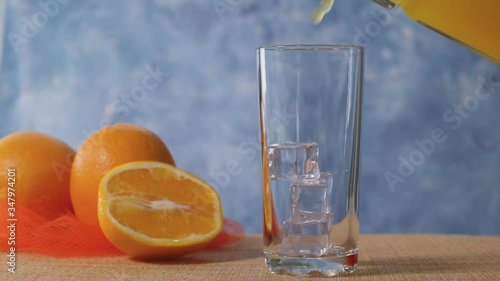 Orange juice is poured into a clear glass with ice in a slow motion