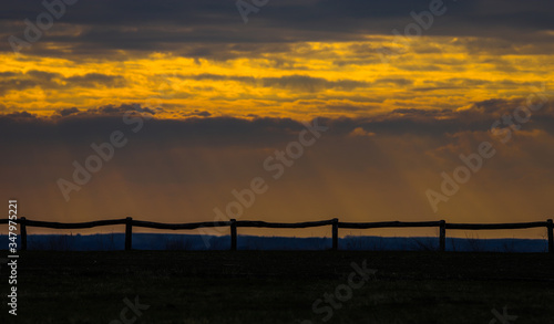 Sunset on a cloudy day with a wooden fence in the foreground.