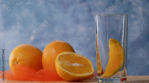 Yellow orange lemonade is poured into a clear glass with orange and ice. Slow motion.