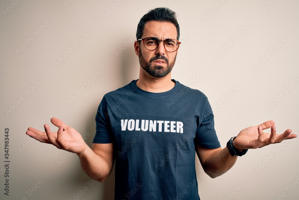 Handsome man with beard wearing t-shirt with volunteer message over white background clueless and confused with open arms, no idea concept. Handsome man with beard wearing t-shirt with volunteer message over white background clueless and confused with open arms, no idea concept.