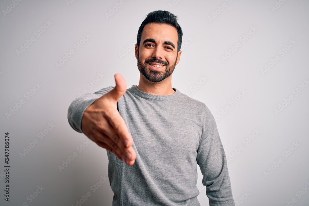 Young handsome man with beard wearing casual sweater standing over white background smiling friendly offering handshake as greeting and welcoming. Successful business. Young handsome man with beard wearing casual sweater standing over white background smiling friendly offering handshake as greeting and welcoming. Successful business.