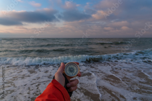 First-person view of a female hand with a compass on a background of a beautiful sea landscape. The concept of navigating the search for your own path and orientation to the cardinal points