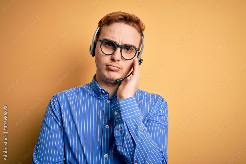 Young handsome redhead call center agent man wearing glasses working using headset thinking looking tired and bored with depression problems with crossed arms.