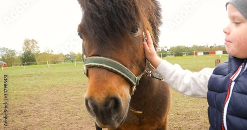 Closeup of a kid stroking a horse. The boy is preparing to learn how to ride a pony in the cold season. Hippotherapy for the development of the baby. A child in a turquoise overalls. Selective focus