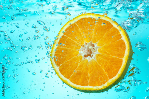 Half an orange is placed in a tank of water that emits bulbs and splash . Close-up.